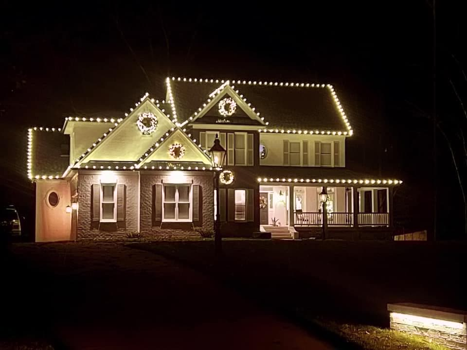 Farmhouse with roofline lights, lit porch, and gable wreaths