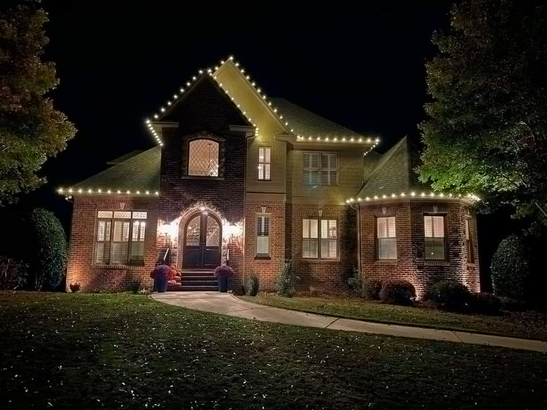 Brick two-story home with warm white roofline lights and lit entry