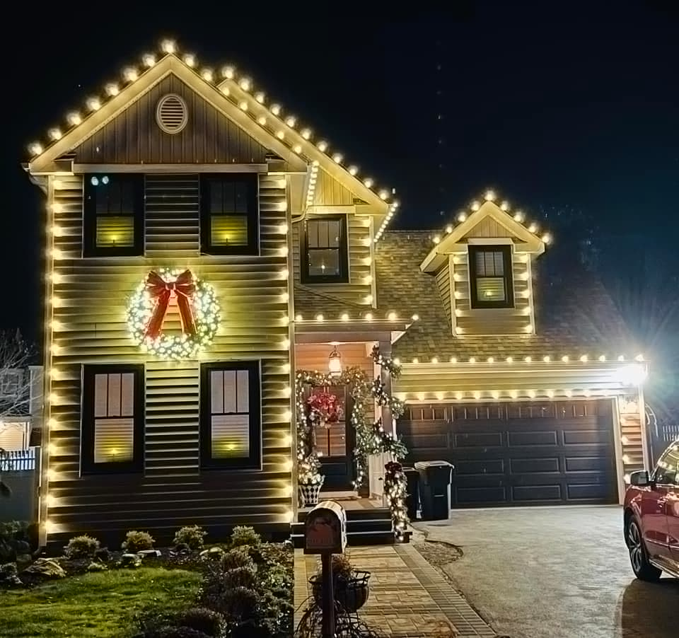 Two-story home with roofline lights, wreath, and lit porch garland
